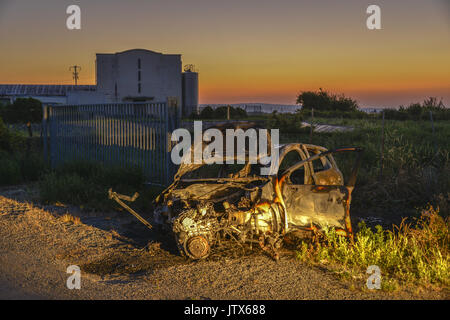 Abbandonata, bruciata auto al tramonto, illuminato da luci auto Foto Stock