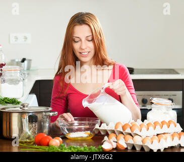 Casalinga in rosso rendere lâ impasto con latte in cucina domestica Foto Stock