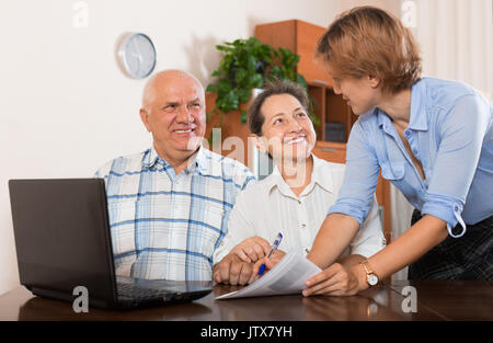 Coppia matura a rispondere alle domande del lavoratore di outreach con notebook in ufficio Foto Stock