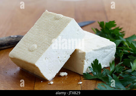 Due blocchi di tofu bianco con prezzemolo fresco e rustico coltello sul tagliere di legno. Foto Stock