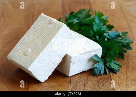 Due blocchi di tofu bianco con prezzemolo fresco sul tagliere di legno. Foto Stock