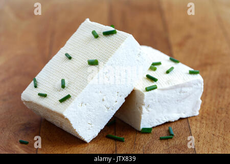 Due blocchi di tofu bianco con erba cipollina fresca sul tagliere di legno. Foto Stock