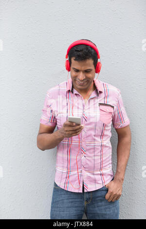 Uomo indiano con uno Smart Phone. Uomo asiatico utilizzando Smart Phone, appoggiata contro un muro grigio. Foto Stock