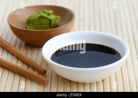 Salsa di soia salsa nella ciotola bianco sul tappetino di bambù con bacchette e wasabi incolla iin ciotola di legno. Foto Stock