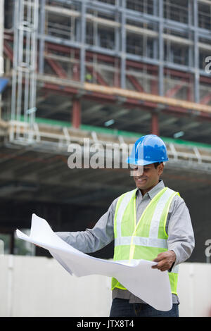 Indian construction manager o di un Architetto controllando il blueprint di piani di un edificio sito. Foto Stock