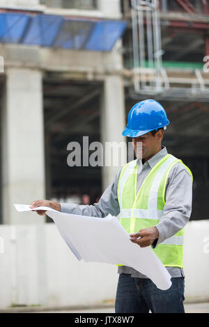 Indian construction manager o di un Architetto controllando il blueprint di piani di un edificio sito. Foto Stock