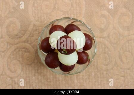 Gulab Jamun e Rasgulla giacente uno sopra l'altro in una ciotola di vetro Foto Stock