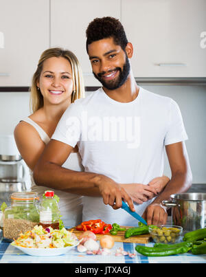 Ritratto di giovane felice interracial giovane Cucina verdure e ridere in cucina Foto Stock