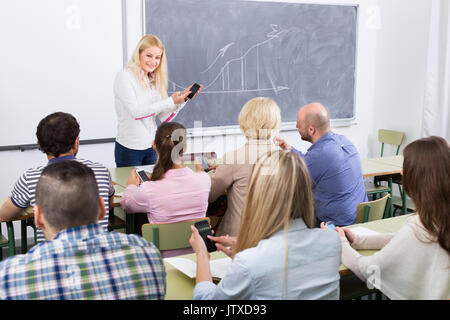 Professionisti di prendere appunti su smartphone alla sessione di formazione per i dipendenti in aula Foto Stock