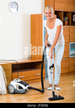 Bionda sorridente ragazza in pantaloncini corti la pulizia con aspirapolvere  sul pavimento in parquet a casa Foto stock - Alamy