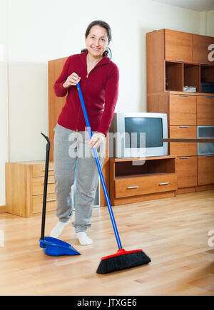 Sorridente donna matura spazzare il pavimento a casa Foto Stock