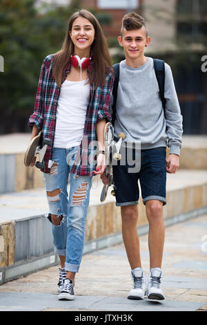 Ritratto di felice sorridente ragazza ragazzo e gli adolescenti a piedi con skateboard all'aperto Foto Stock