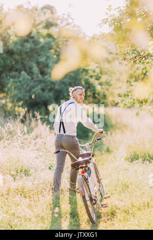 La vista posteriore del moderno abito sposo tenendo la bicicletta in primavera soleggiata foresta. Foto Stock