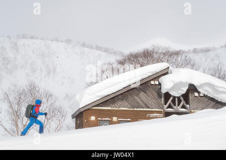 Un backcountry rider davanti a un giapponese di casa in legno, sepolta sotto uno spesso strato di neve. Hokkaido è famosa per la polvere e lo sci backcountry. Foto Stock