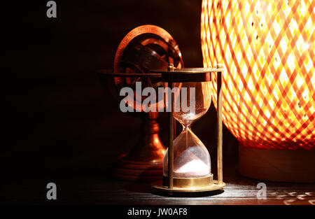 Vintage ancora in vita. Vicino a clessidra ottone antico globo e lampada incandescente su sfondo scuro Foto Stock