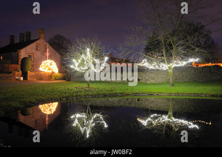 Le luci di Natale decorano alberi intorno al laghetto in Foolow, un pittoresco villaggio nel Peak District,Derbyshire,Inghilterra Regno Unito - Dicembre Foto Stock