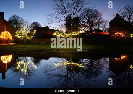 Le luci di Natale decorano alberi intorno al laghetto in Foolow, un pittoresco villaggio nel Peak District,Derbyshire,Inghilterra Regno Unito - Dicembre Foto Stock