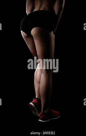 Bassa sezione di sportive in posa di sportswear e mostrando la sua gambe muscolare isolato su nero Foto Stock