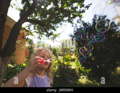 Carino bambina sta soffiando una bolle di sapone Foto Stock