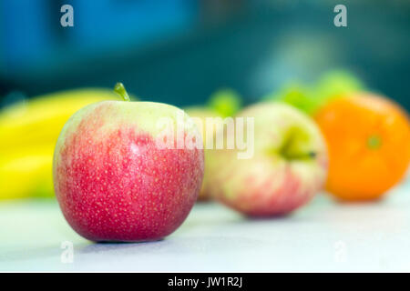 Manzana roja en meza con otras frutas desenfocadas, alimento saludable y naturale vitaminas biella, baja en calorías, apetecible y jugosa, de clima frío Foto Stock