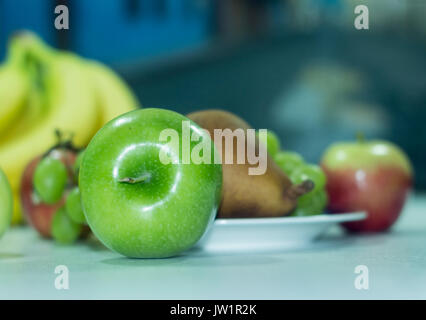 Manzana verde en meza con otras frutas desenfocadas, alimento saludable y naturale vitaminas biella, baja en calorías, apetecible y jugosa, de clima frío Foto Stock