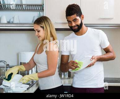 Felice american uomo nero con sorridente donna bianca spolvero in cucina domestica Foto Stock