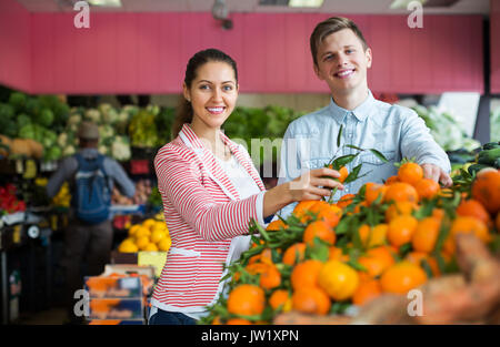 Due giovani felici i clienti che acquistano le arance, limoni e mandarini nella sezione di negozi di generi alimentari Foto Stock