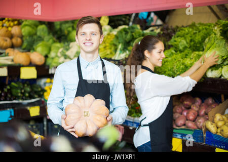 Roba sorridente nel grembiule vendita di zucca dolce al marketplace Foto Stock