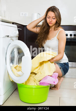 Home servizio lavanderia. Stanco giovane femmina con vestiti vicino alla macchina di lavaggio a casa Foto Stock