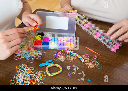 Primo piano delle donne rendendo i braccialetti decorativi con fasce elastiche a tavola Foto Stock