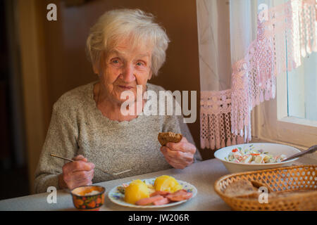 Una donna anziana mangia seduto al tavolo. Foto Stock
