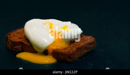 Uovo in camicia su una fetta di pane integrale. Foto su uno sfondo nero Foto Stock