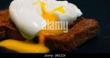 Uovo in camicia su una fetta di pane integrale. Foto su uno sfondo nero Foto Stock
