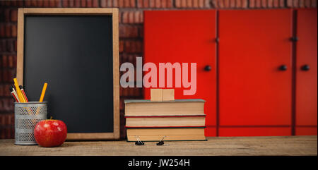 Libri di ardesia con desk organizer e Apple su un tavolo di legno contro chiuso armadietti arancione contro un muro di mattoni Foto Stock