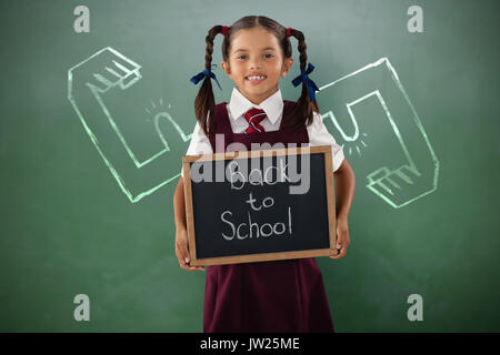 Sorridente schoolgirl tenendo la scrittura di ardesia verde contro la lavagna Foto Stock