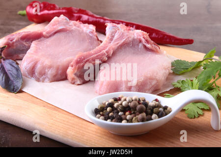 Materie bistecca di carne di maiale con spezie foglie di coriandolo sul tagliere di legno. Pronta per la cottura. Foto Stock