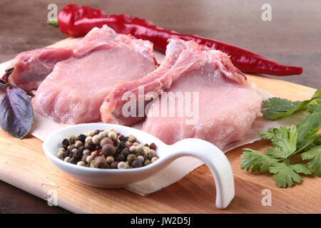 Materie bistecca di carne di maiale con spezie foglie di coriandolo sul tagliere di legno. Pronta per la cottura. Foto Stock