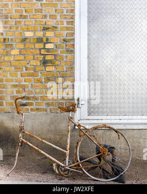 Vecchio arrugginito con bici mancante ruota anteriore appoggiata contro un muro di mattoni. Rimosso dalla bocca di ingresso o di uscita della centrale idroelettrica Floda, Svezia. Modello di Rilascio: No. Proprietà di rilascio: No. Foto Stock