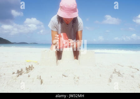 Stati Uniti d'America, USVI, San Giovanni, donna matura in rosa cappello per il sole rendendo sandcastle sulla spiaggia Foto Stock