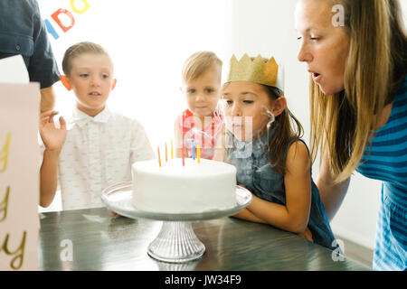 Fratelli (2-3, 6-7) guardando la sorella (6-7) e madre di soffiaggio candele di compleanno Foto Stock