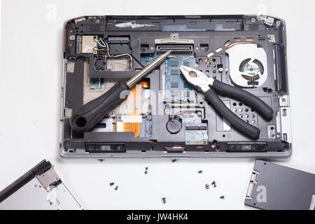 Le parti interne, componenti e pezzi di rottura di un computer portatile con un cacciavite e pinza su sfondo bianco con copia spazio in un techn Foto Stock