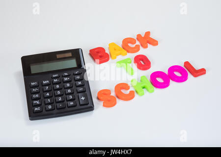 Si torna a scuola scritta in alfabeto lettere di apprendimento a fianco di una calcolatrice con sfondo bianco e copia di spazio. Foto Stock