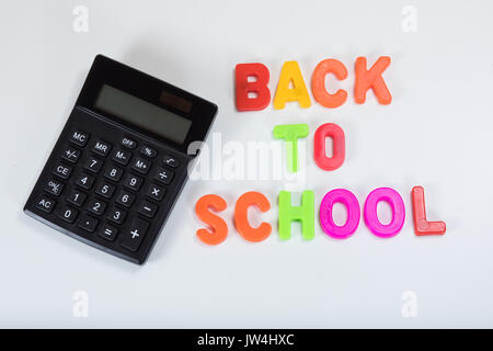 Si torna a scuola scritta in alfabeto lettere di apprendimento a fianco di una calcolatrice con sfondo bianco e copia di spazio. Foto Stock