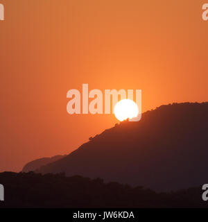 Paesaggio minimalista con sagome di creste montane e orange sky con Sun in estate a bright sunset.incredibile vista sulle colline e il disco solare Foto Stock