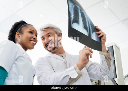 Basso angolo di vista sorridente maschio e femmina radiologi analizzando i raggi X al torace nella sala esame Foto Stock