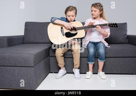 Focalizzato il fratello e la sorella gioca su chitarra insieme mentre è seduto sul divano Foto Stock