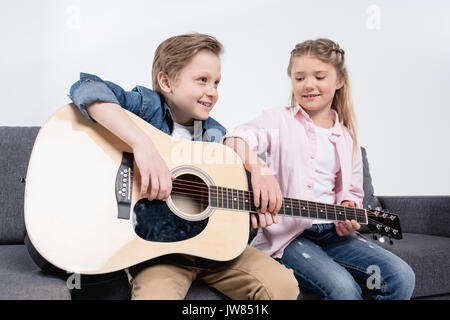 Felice fratello e sorella gioca su chitarra insieme mentre è seduto sul divano Foto Stock
