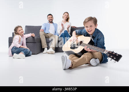 Genitori felici e carino sorellina guardando sorridente ragazzo a suonare la chitarra Foto Stock