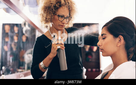 Donna parrucchiere capelli di spruzzatura liquido di impostazione sul suo cliente i capelli. Giovane donna ottenendo un elegante taglio di capelli fatto a salon. Foto Stock