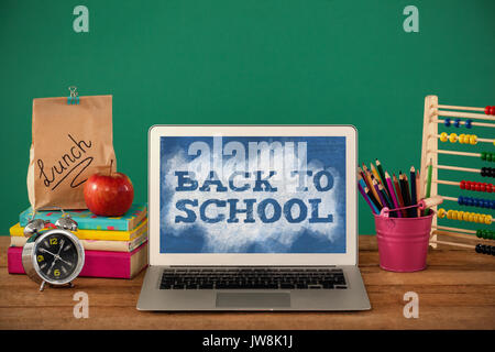 Si torna a scuola del testo in verde e blu splash contro forniture scolastiche con computer portatile sul tavolo di legno Foto Stock